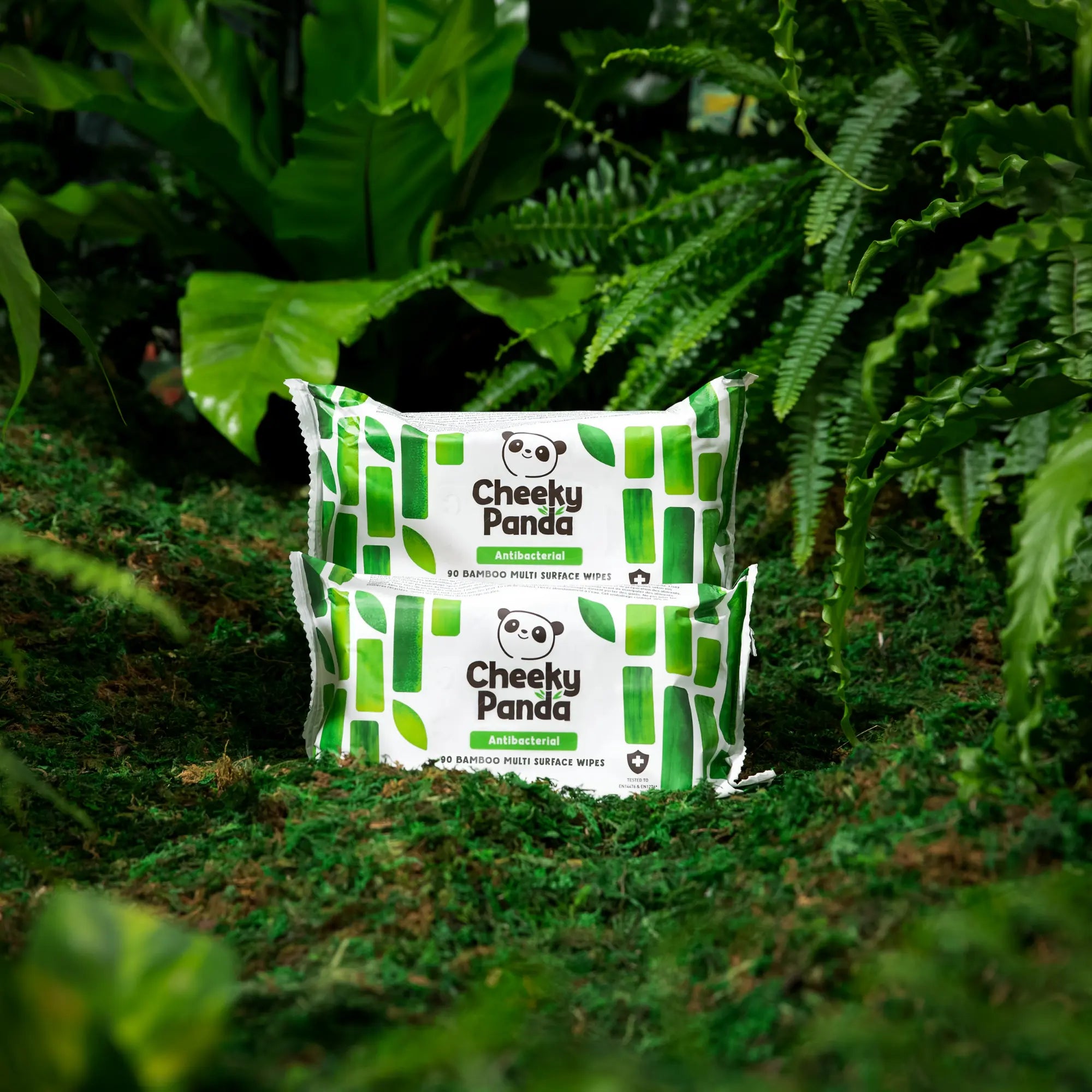 Two packs of Cheeky Panda antibacterial bamboo multi-surface wipes nestled in lush green foliage.