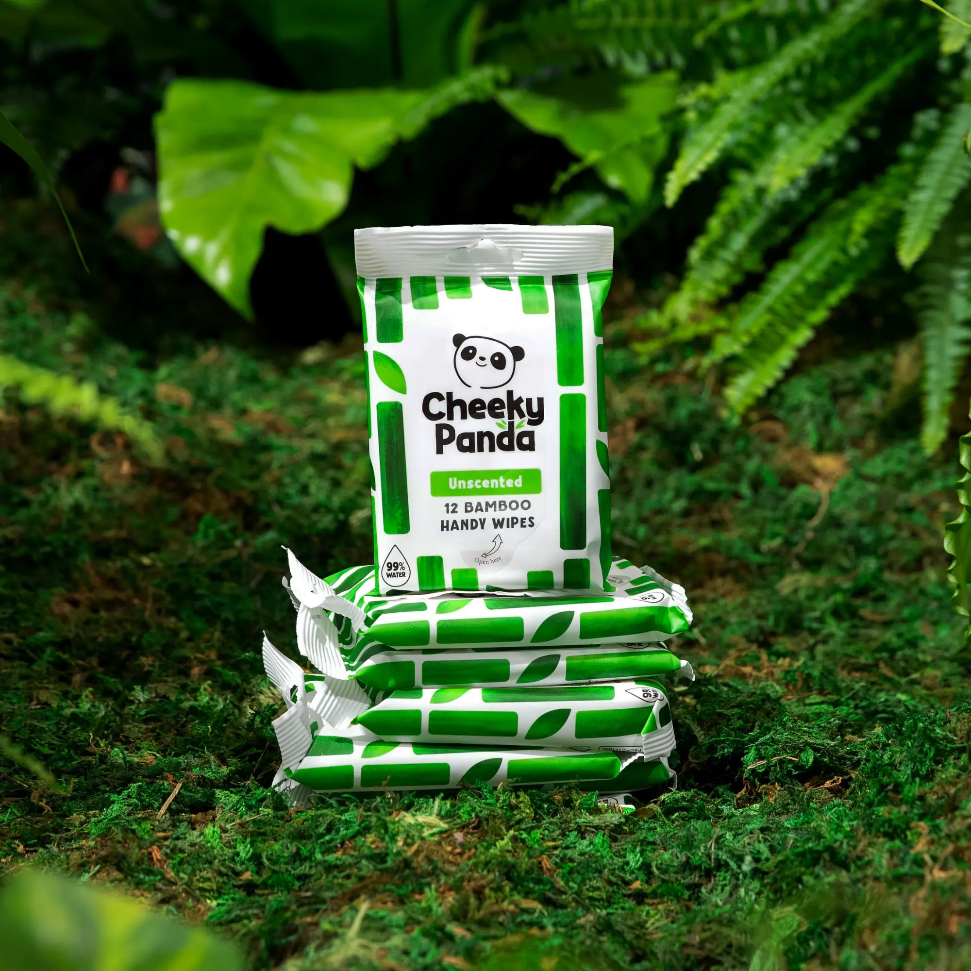 Stack of Cheeky Panda Unscented 12 Handy Wipes packs in a natural, mossy setting.