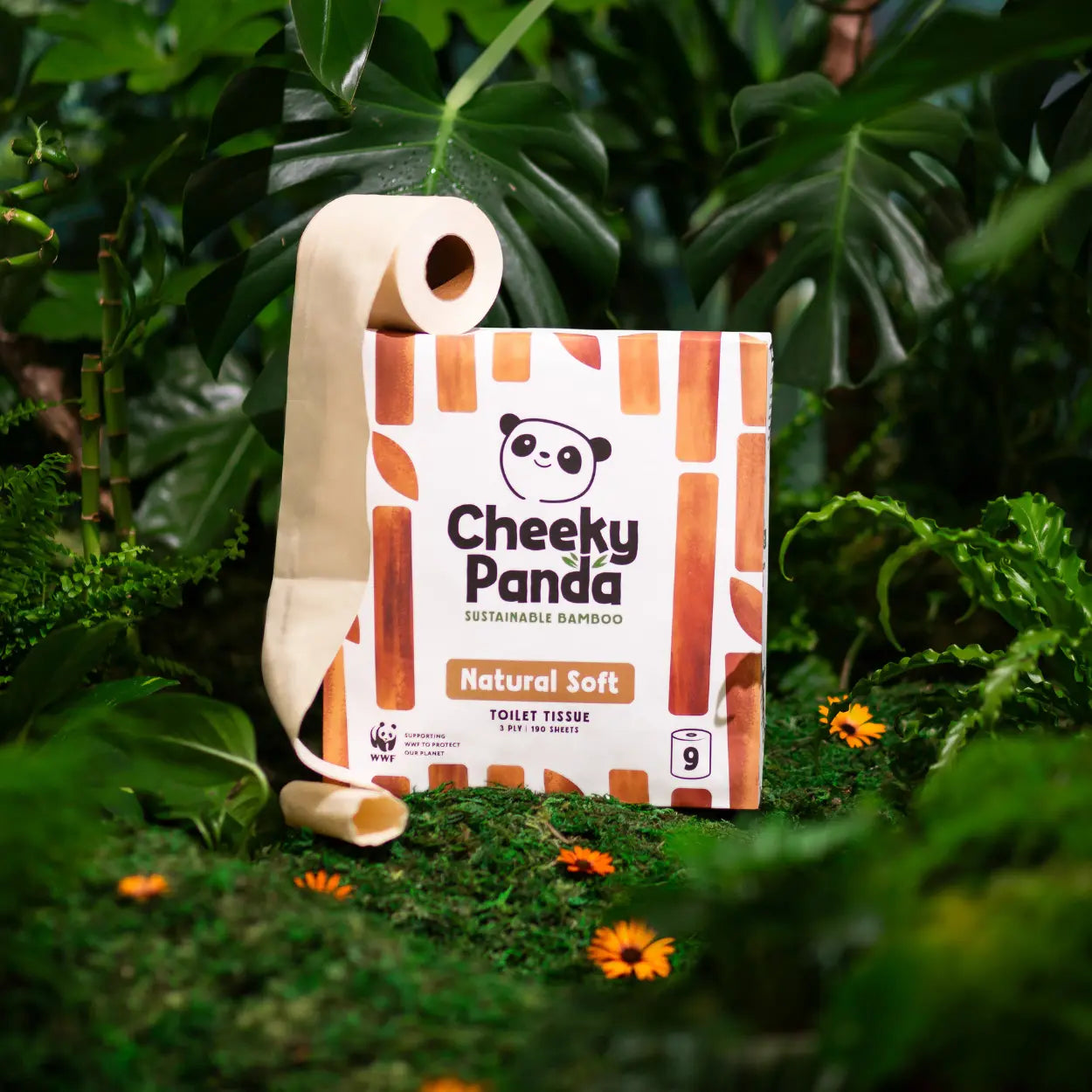 Cheeky Panda unbleached sustainable bamboo toilet tissue package in a natural setting with green leaves and flowers.